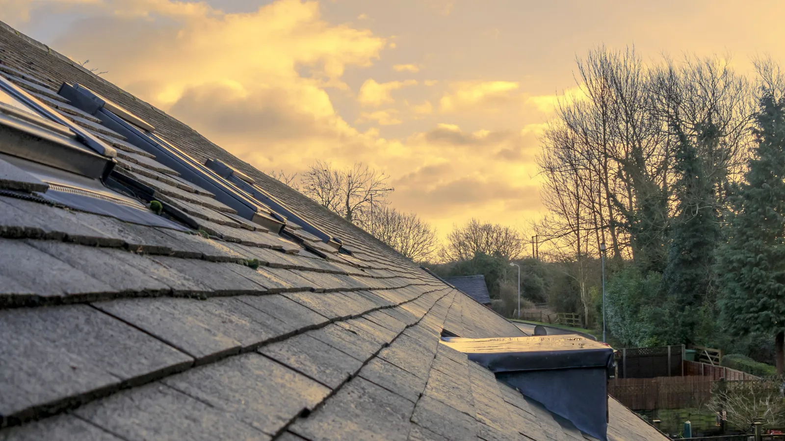 Warm sunset clouds above a shingled roof slope and skylights