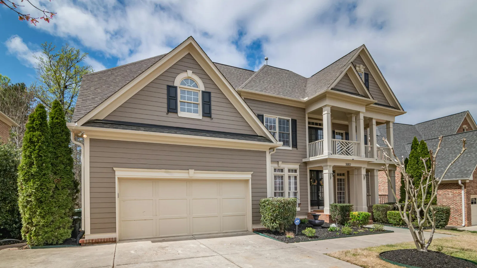 Columned balcony and brown asphalt shingle roof on a tan two-story home